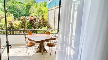 Un balcon avec une table et des chaises, une vue sur la verdure et un bâtiment en arrière-plan.