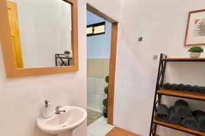 Un bagno con lavandino, specchio e ripiano con asciugamani arrotolati.