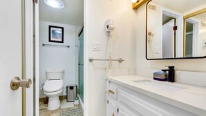Un baño con inodoro, secamanos, lavamanos, espejo y un cubo de basura.