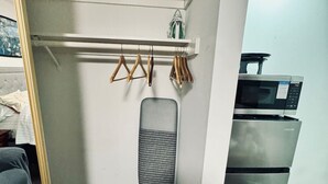 Una habitación con un armario blanco, una percha con ropa, microondas y refrigerador.