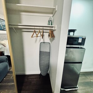 Een kamer met een witte kast, een kledingrek met kleren, een magnetron en een koelkast.