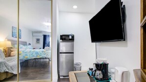 Habitación de hotel con cama, refrigerador, cafetera, televisor y mesita de noche.
