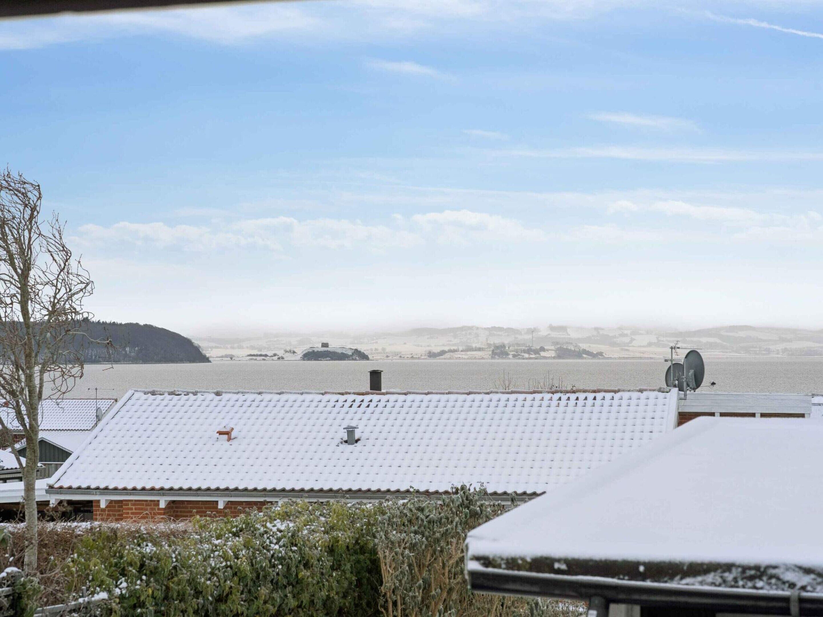 Et boligområde med sneklædte tage, en klar himmel og et fjerntliggende vandareal.