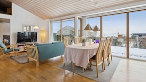 A spacious living area with a large TV, comfortable seating, a dining table, and large windows offering a view of the outdoors. - 4 Star Holiday Home in Ronde (Ronde)