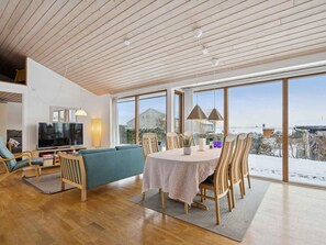 A spacious living area with a large TV, comfortable seating, a dining table, and large windows offering a view of the outdoors. - 4 Star Holiday Home in Ronde (Ronde)