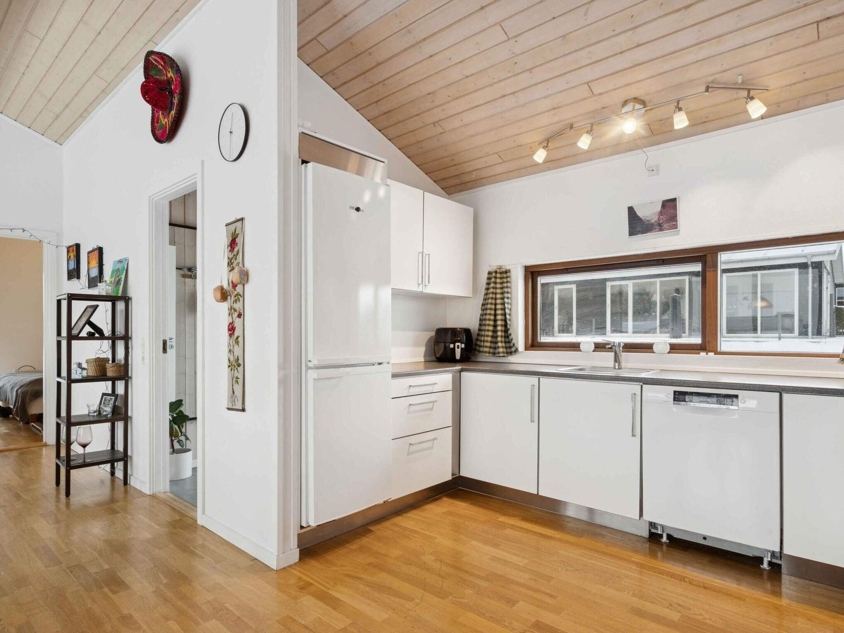 Una cocina moderna con armarios blancos, techo de madera y ventana con vistas.