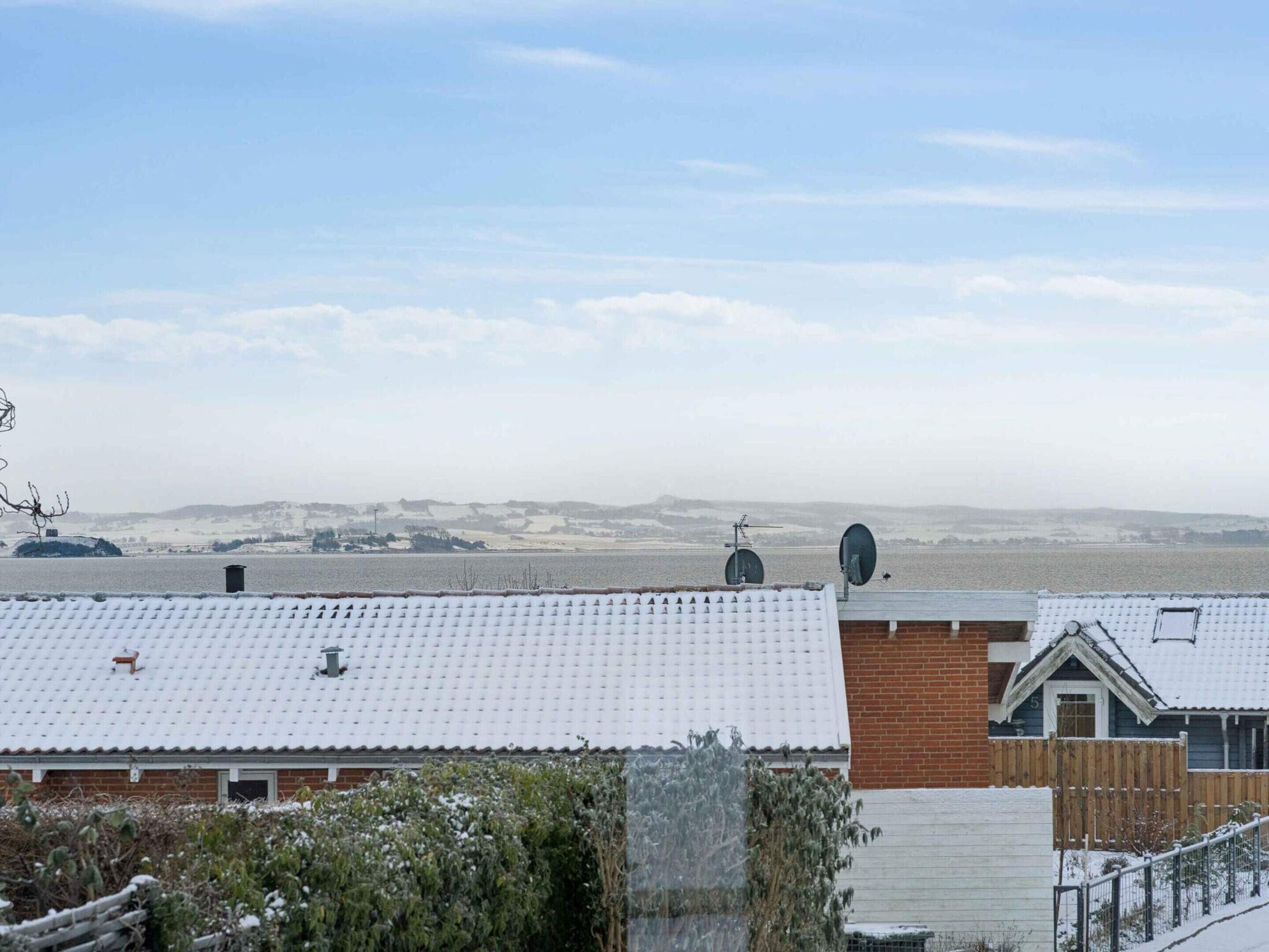 A residential area with snow-covered roofs, satellite dishes, and a distant view of a hilly landscape.