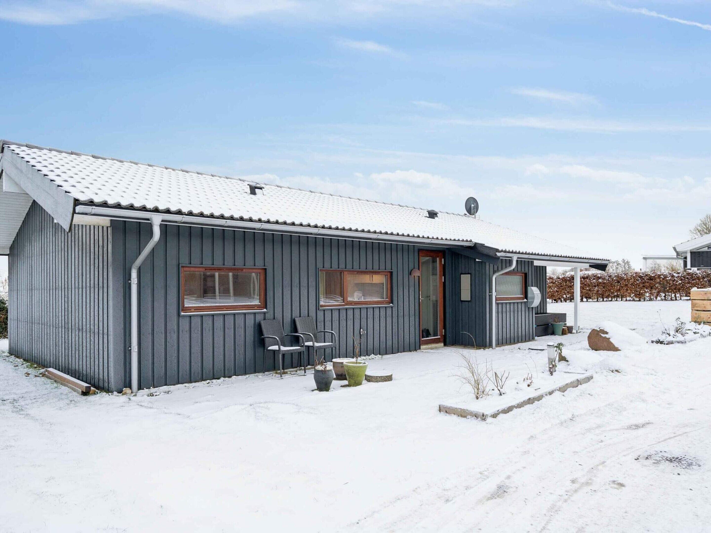 A single-story building with a metal exterior, a tiled roof, and a small porch with chairs.