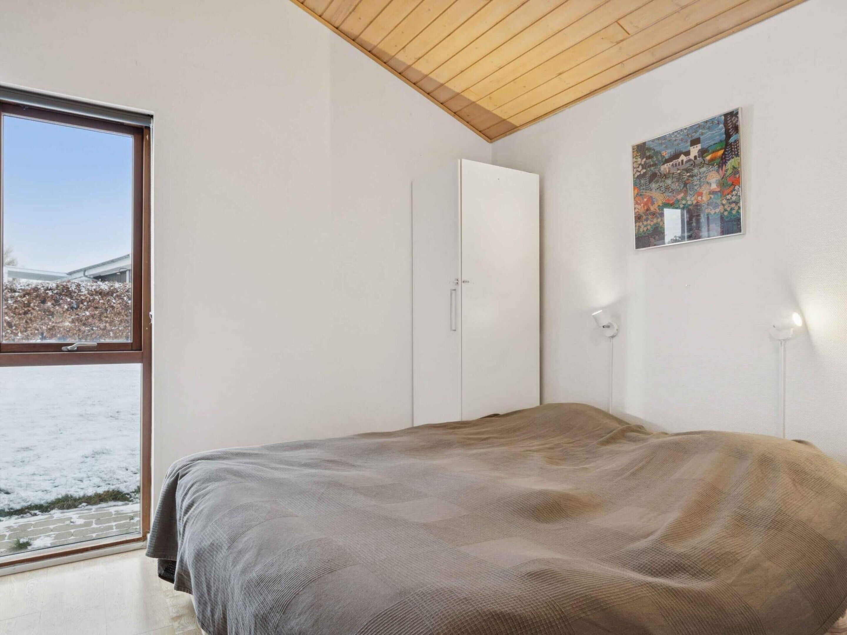 A bedroom with a large window, a bed, a wardrobe, and a painting on the wall.
