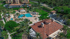 Ein Luftbild eines Resorts mit Swimmingpool, Palmen und einem Gebäude mit rotem Ziegeldach.