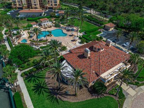 Luchtbeeld van een resort met een zwembad, palmbomen en een gebouw met een rode pannendak.