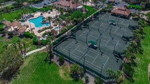 Eine Vogelperspektive zeigt ein Resort mit Schwimmbad, Tennisplätzen und umgebender Grünfläche.