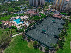 Luchtbeeld van een resort met een zwembad, tennisbanen en omliggend groen.