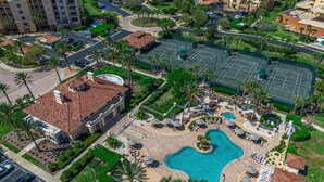 Luftaufnahme eines Resorts mit Swimmingpool, Palmen und Parkplatz.