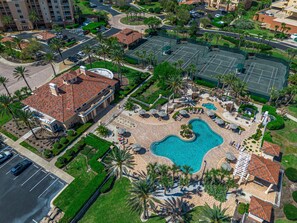 Luchtbeeld van een resort met een zwembad, palmbomen en een parkeerplaats.
