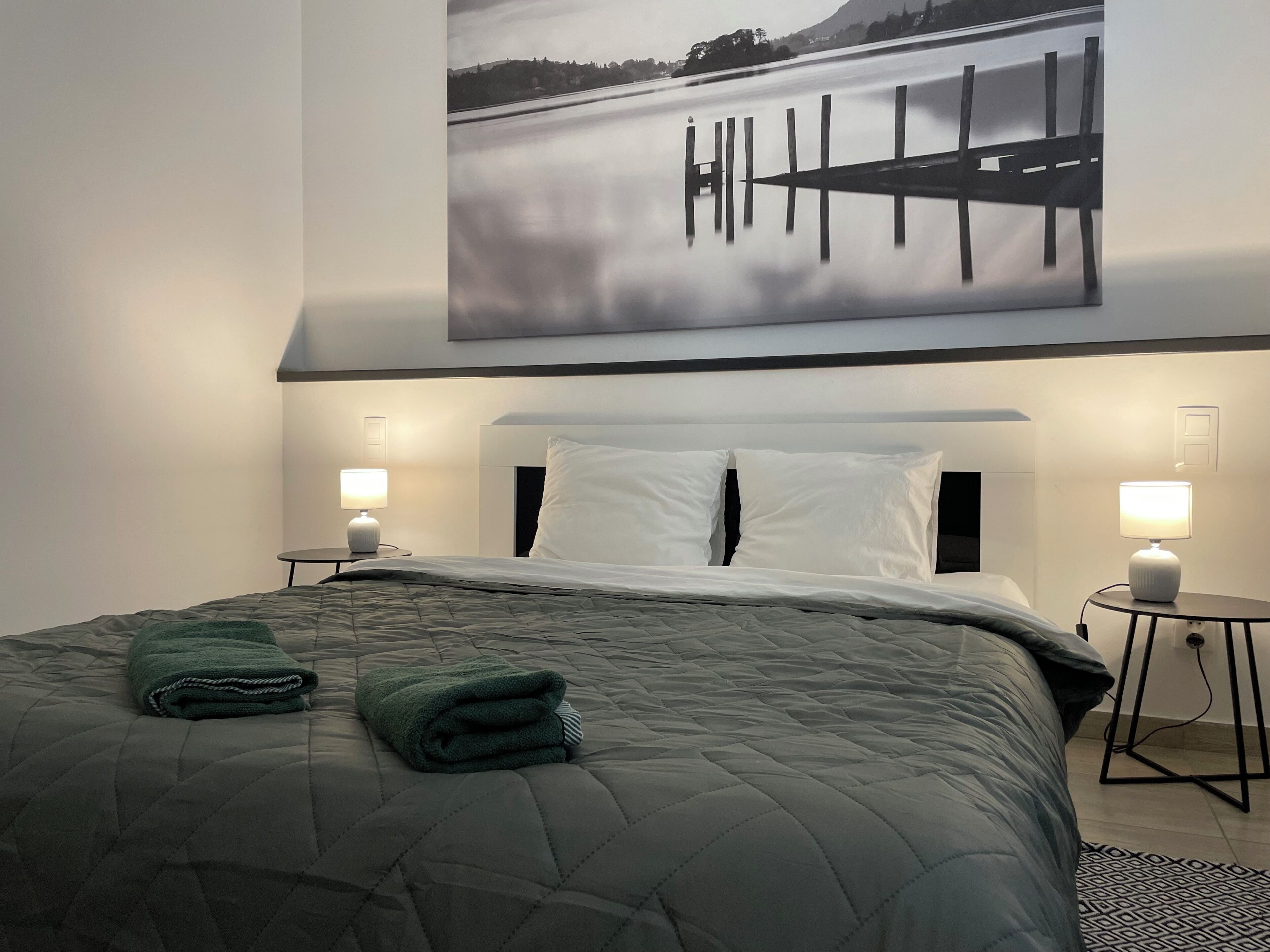 Ein Hotelzimmer mit einem Bett, zwei Nachttischlampen, einem Bild von einem See und einem grünen Handtuch auf dem Bett.