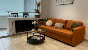 Una sala de estar con un sofá, una mesa de centro, un radiador, una ventana con persianas y un cuadro en la pared.