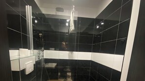 Un baño moderno con cabina de ducha de vidrio, tapa de inodoro de madera y suelo con baldosas blanco y negro.