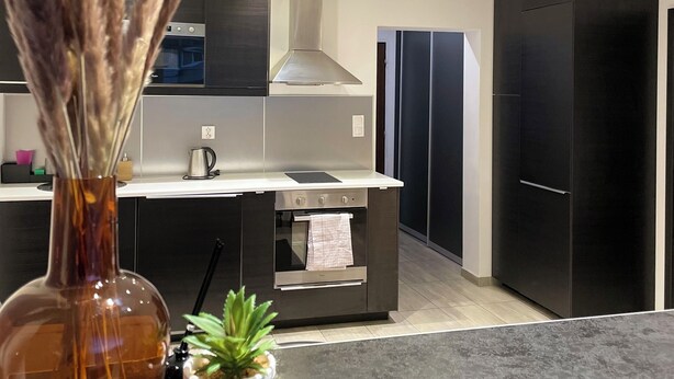 Una cocina moderna con una isla central, electrodomésticos de acero inoxidable y un jarrón decorativo con plantas secas.
