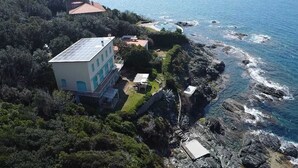 Una propiedad costera con un edificio grande, piscina y terreno rocoso.
