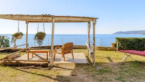 Una pérgola de madera con una silla de mimbre y una mesa, con vistas al mar.