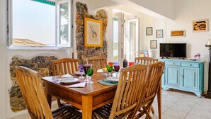 Un comedor con pared de piedra, sillas de madera, una mesa de madera y un televisor sobre un mueble.
