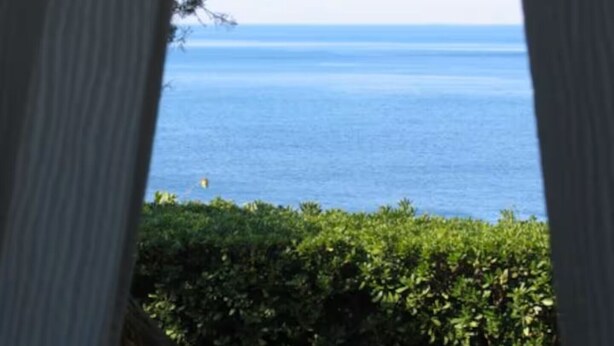 Vista a través de una ventana con cielo azul despejado y una masa de agua en la distancia.