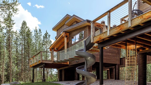 Una casa moderna de madera con una escalera espiral, una terraza y un paisaje boscoso de fondo.