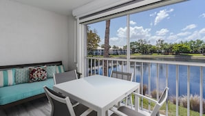 En balkon med hvidt bord og stole, med udsigt over vand og grønt.