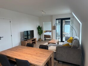 A modern living room with a wooden dining table, a sofa, a TV, and a large window. - Modern Apartment Hasselt 2p (Hasselt)