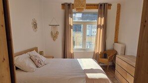 A bedroom with a bed, wooden dresser, wicker chair, and a window with curtains. - Cocon Bohème Le Portel House 12 pers(+2) beach 15 min walk (Le Portel)