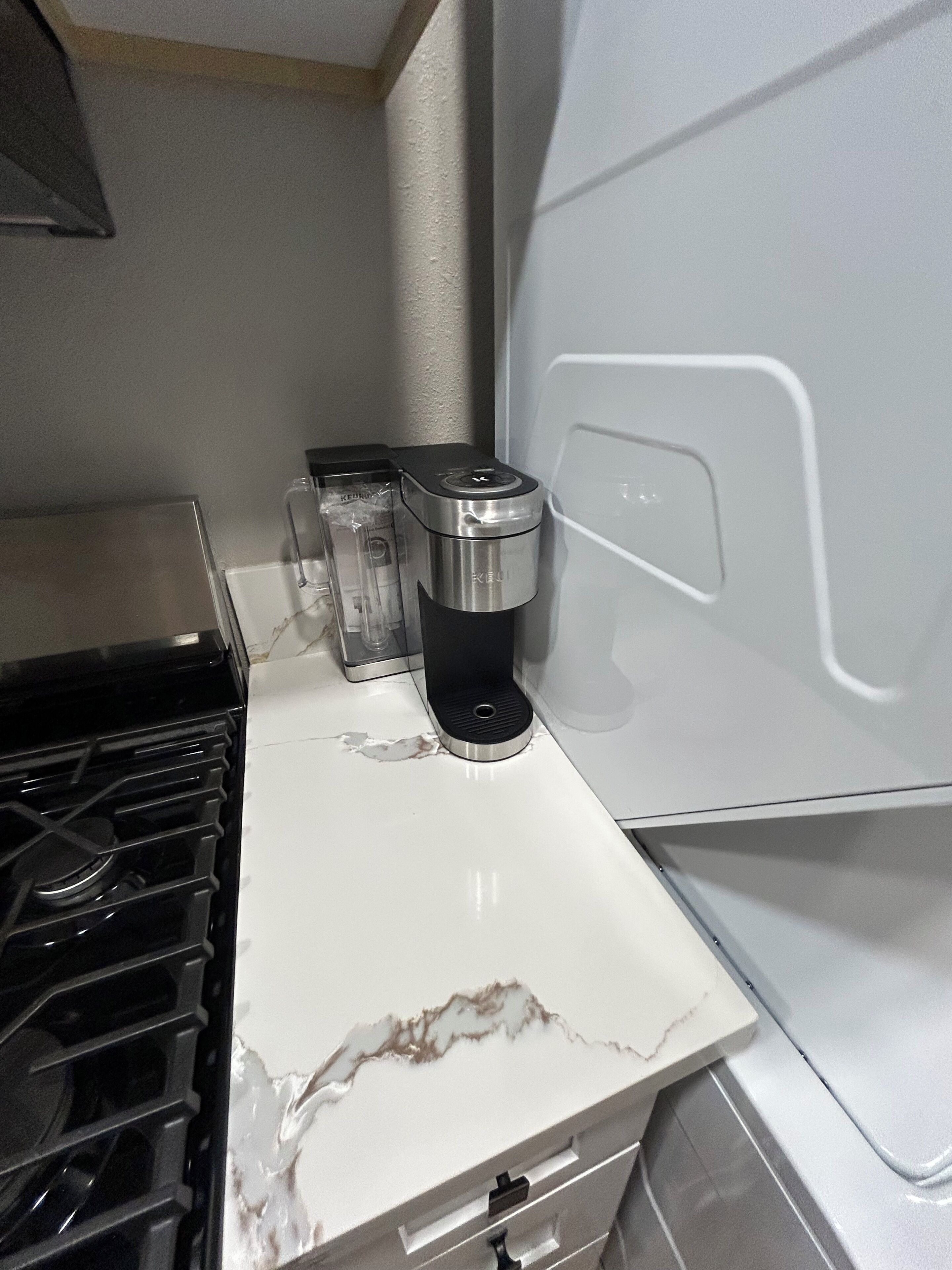 Et køkken med en hvid bordplade, kaffemaskine og komfur.