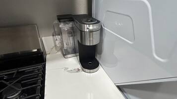 Et køkken med en hvid bordplade, kaffemaskine og komfur.