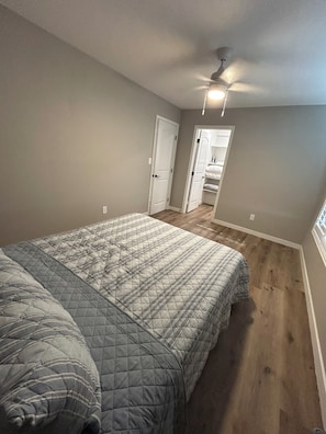 Une chambre à coucher avec un lit, un ventilateur de plafond et une porte donnant sur une autre pièce.