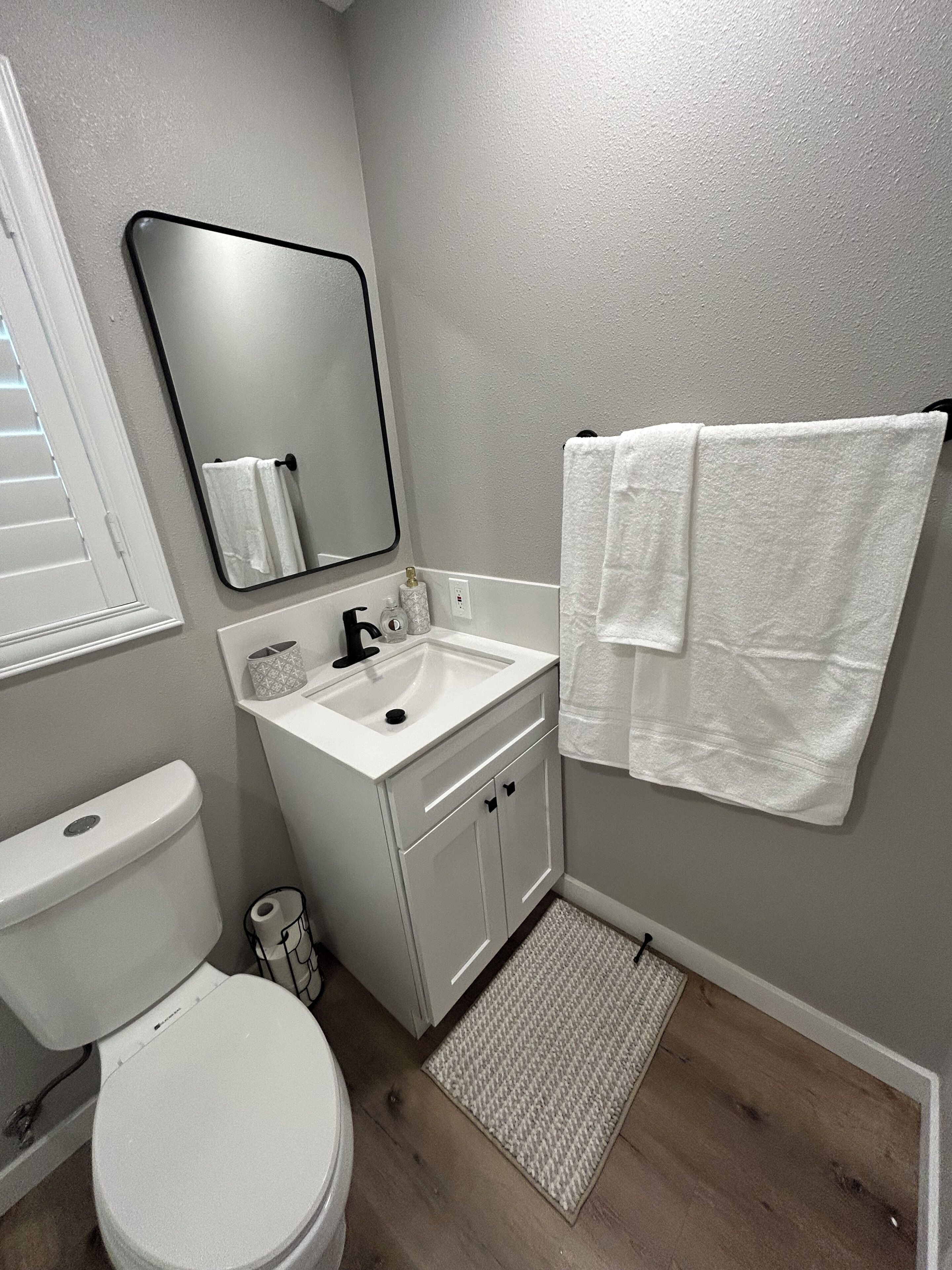 A bathroom with a toilet, sink, mirror, and two towels hanging on the wall.