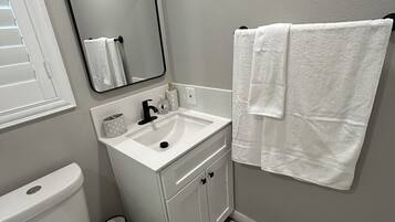 A bathroom with a toilet, sink, mirror, and two towels hanging on the wall.