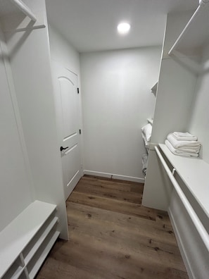 Une petite pièce étroite aux murs blancs, avec un plancher en bois, une porte blanche et une étagère blanche où sont pliées des serviettes.