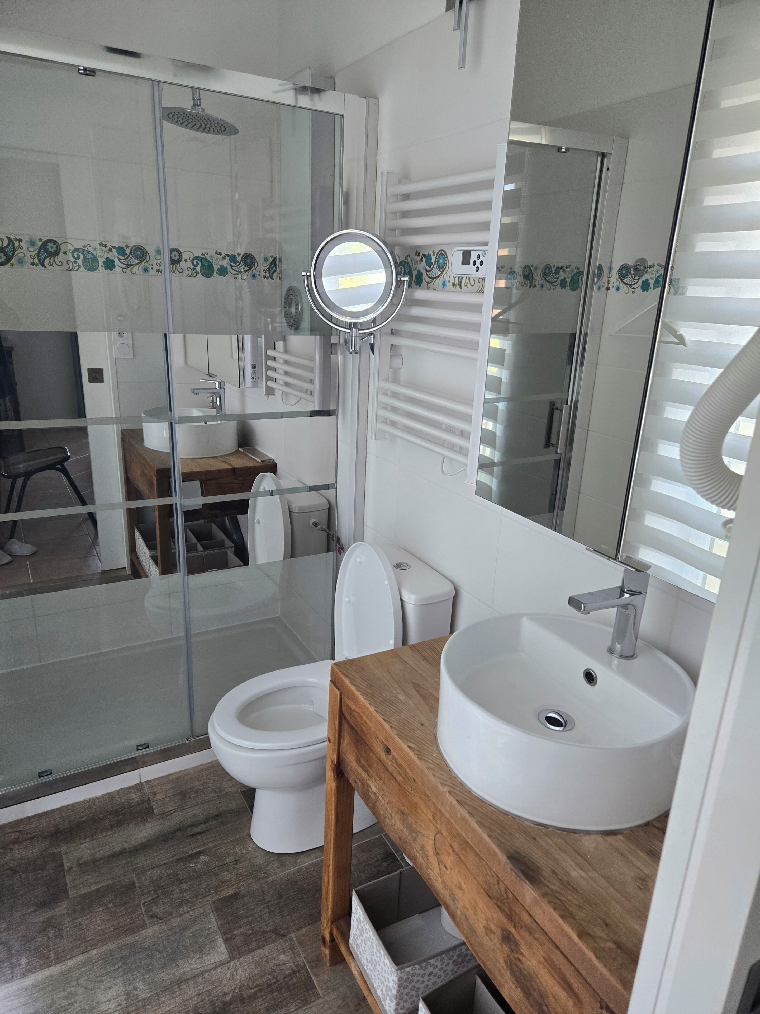 A modern bathroom with a glass shower enclosure, a toilet, a sink with a wooden vanity, and a large mirror.