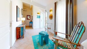 A hallway with a blue stool, a wooden chair, and a console table with artwork. - La  parenthèse de Villepey (Fréjus)