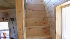 A wooden staircase in a cabin with a window on the right and a table with a lamp on the left.