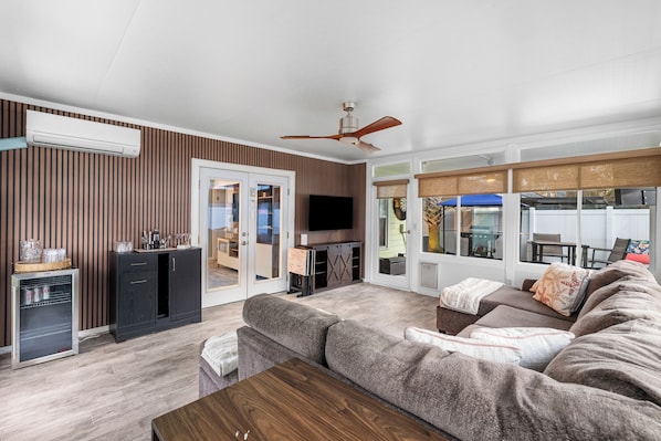 A living room with a sofa, a coffee table, a TV, and a ceiling fan. - 3BR Pool & Hot Tub Retreat | Good Morning Rentals (Jacksonville Beach)