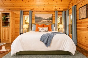 A wooden cabin bedroom with a large bed, a wooden wardrobe, and a painting on the wall. - Private hot tub and fireside evenings for two (Broken Bow)