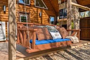 A wooden swing chair with patterned cushions, a stone wall, and a wooden deck. - Private hot tub and fireside evenings for two (Broken Bow)