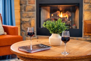 A round wooden table with two wine glasses and a book, a potted plant, and a fireplace in the background. - Private hot tub and fireside evenings for two (Broken Bow)