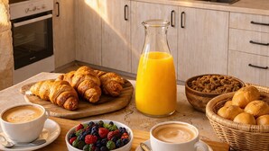 Frühstücksaufteilung mit Croissants, Obst, Kaffee und Orangensaft in einer Küche mit Steinbögen und Kamin aus Stein.