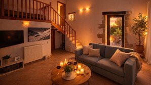 Ein geräumiges Wohnzimmer mit Treppe, einer Couch, einem Couchtisch mit Kerzen und einem an der Wand befestigten Fernseher.