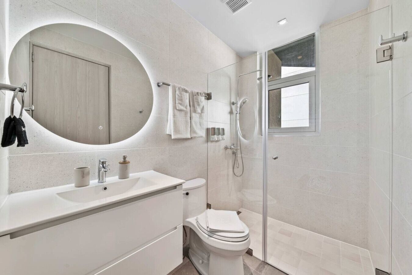 A modern bathroom with a curved vanity, a toilet, a shower enclosure, and a large mirror.