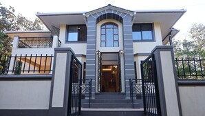 A modern two-story house with a symmetrical facade, a central entrance with a staircase, and a gated driveway.