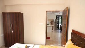 A bedroom with a bed, a wardrobe, and a view into a kitchen area.