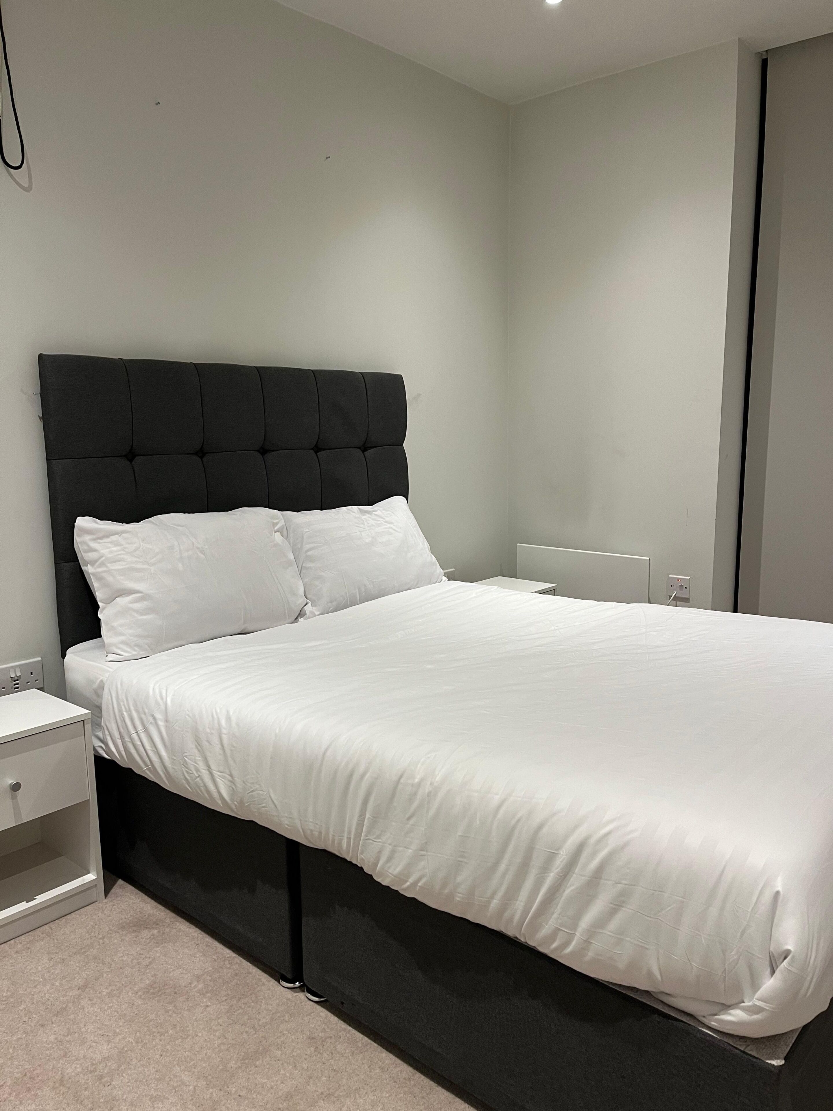 Quarto moderno com uma cama grande, mesa de cabeceira e luminária fixada na parede.
